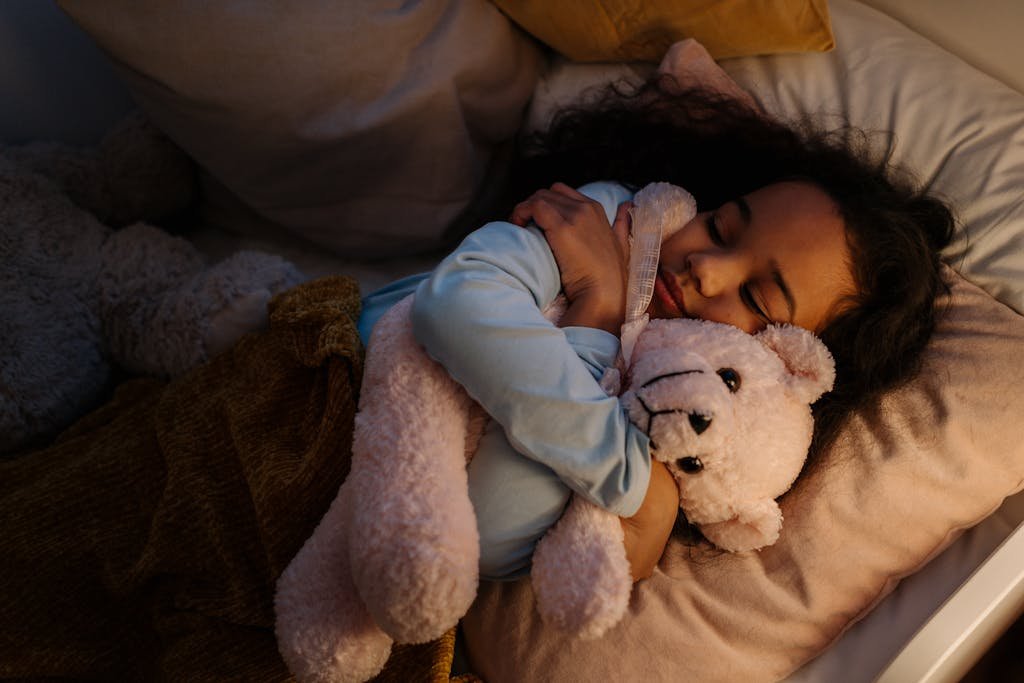 A young girl peacefully sleeping, hugging a teddy bear in her bed with soft pillows and blankets.