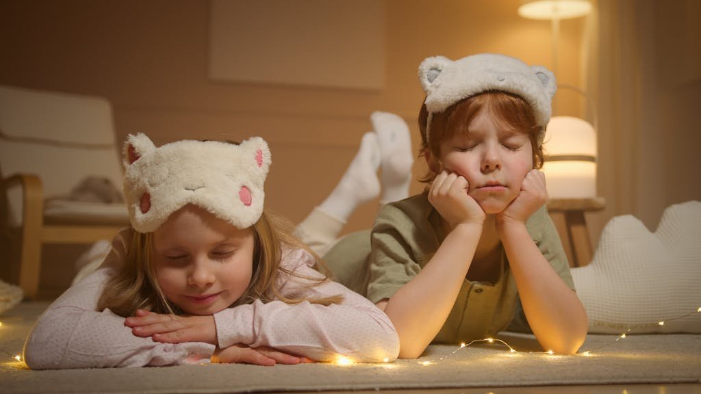 Cute children wearing animal-themed sleep masks, resting indoors during bedtime.