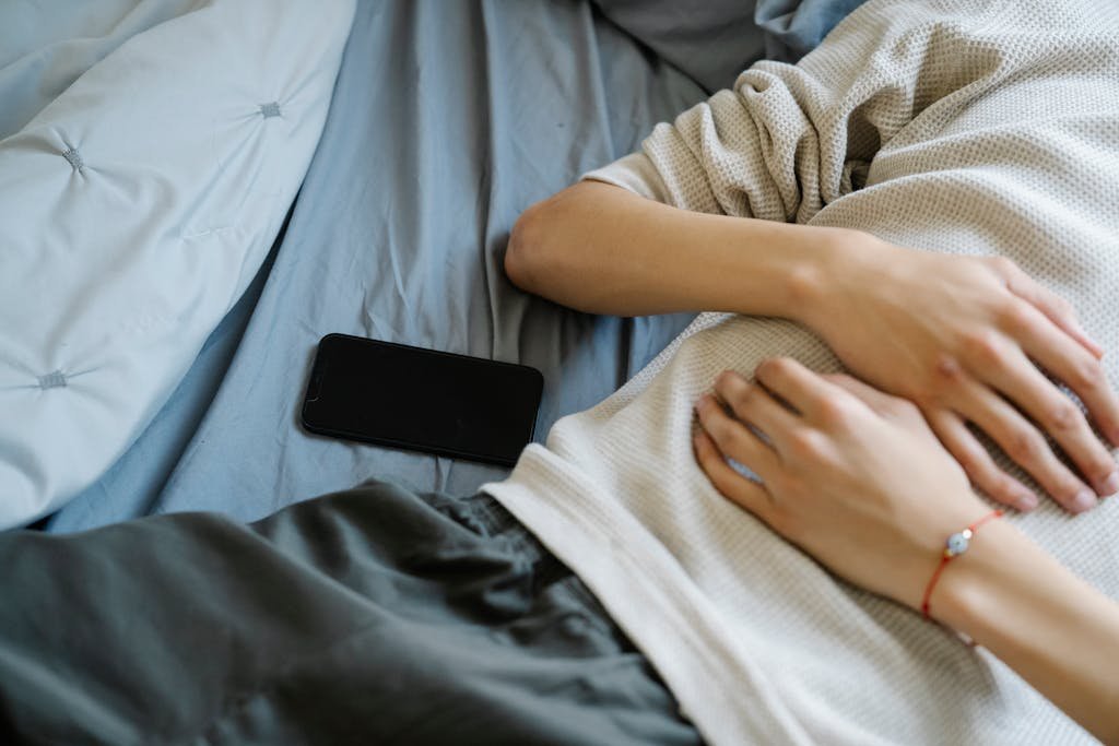 A young adult lying on a bed next to a smartphone, capturing a moment of relaxation and technology use.